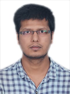 A young man in glasses writes in a notebook while sitting on a stylish couch indoors.