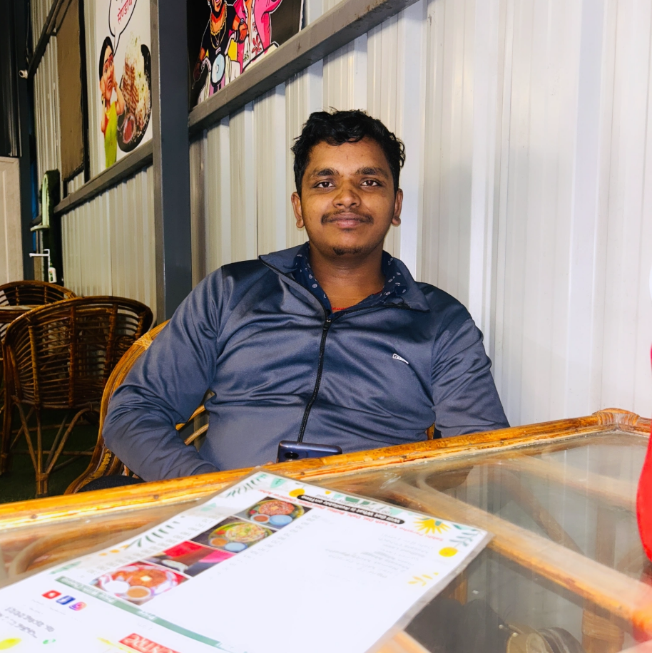 A young man in glasses writes in a notebook while sitting on a stylish couch indoors.