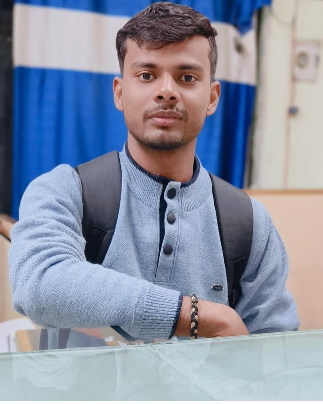 A young man in glasses writes in a notebook while sitting on a stylish couch indoors.